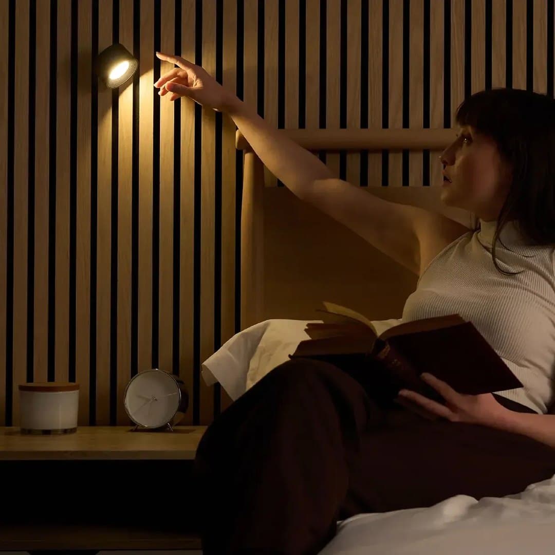 Une femme allume la lampe murale aimantée au-dessus de son lit